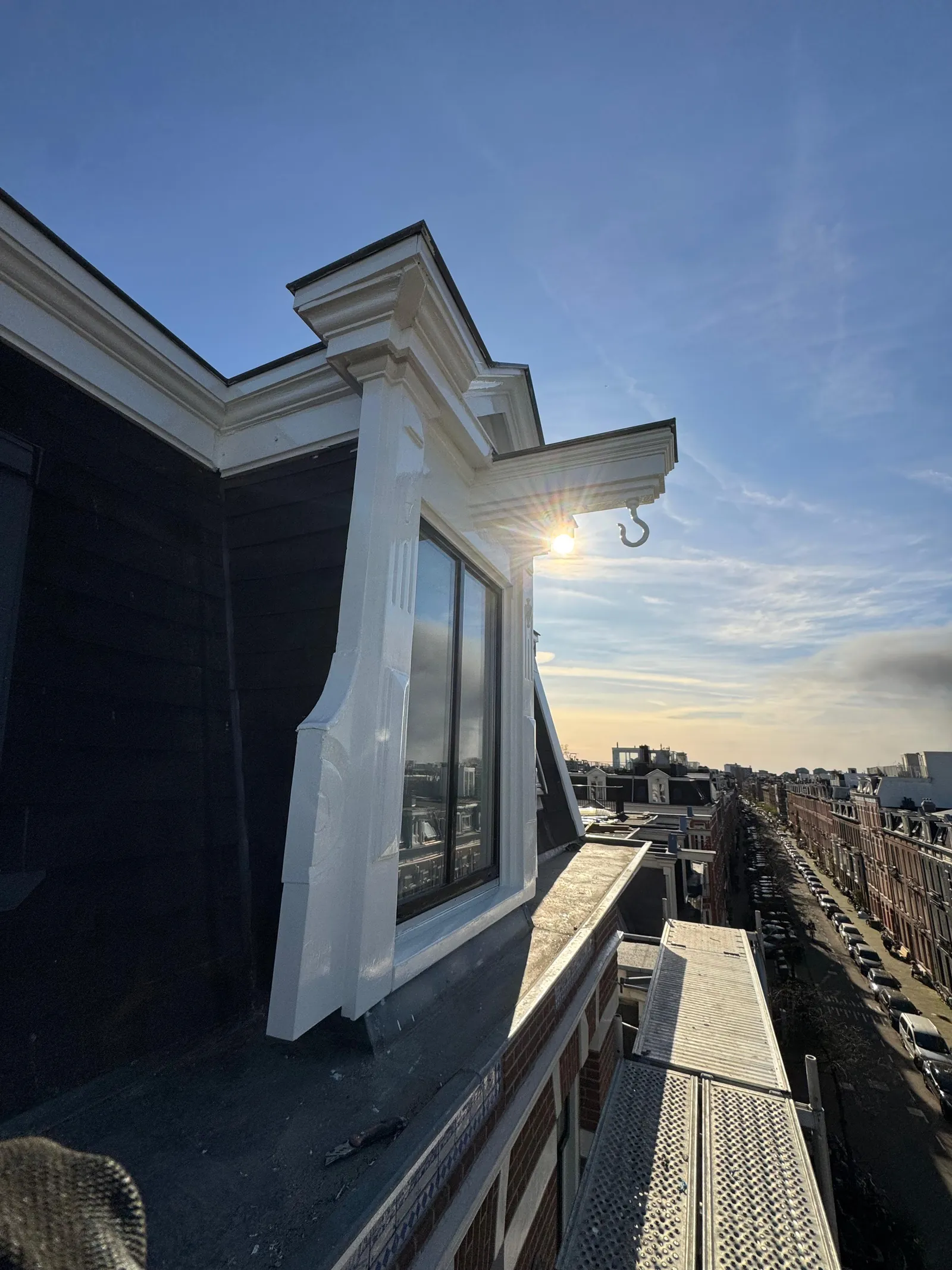 Strak wit geschilderde dakkapel met kroonlijst bij zonsondergang boven Amsterdam